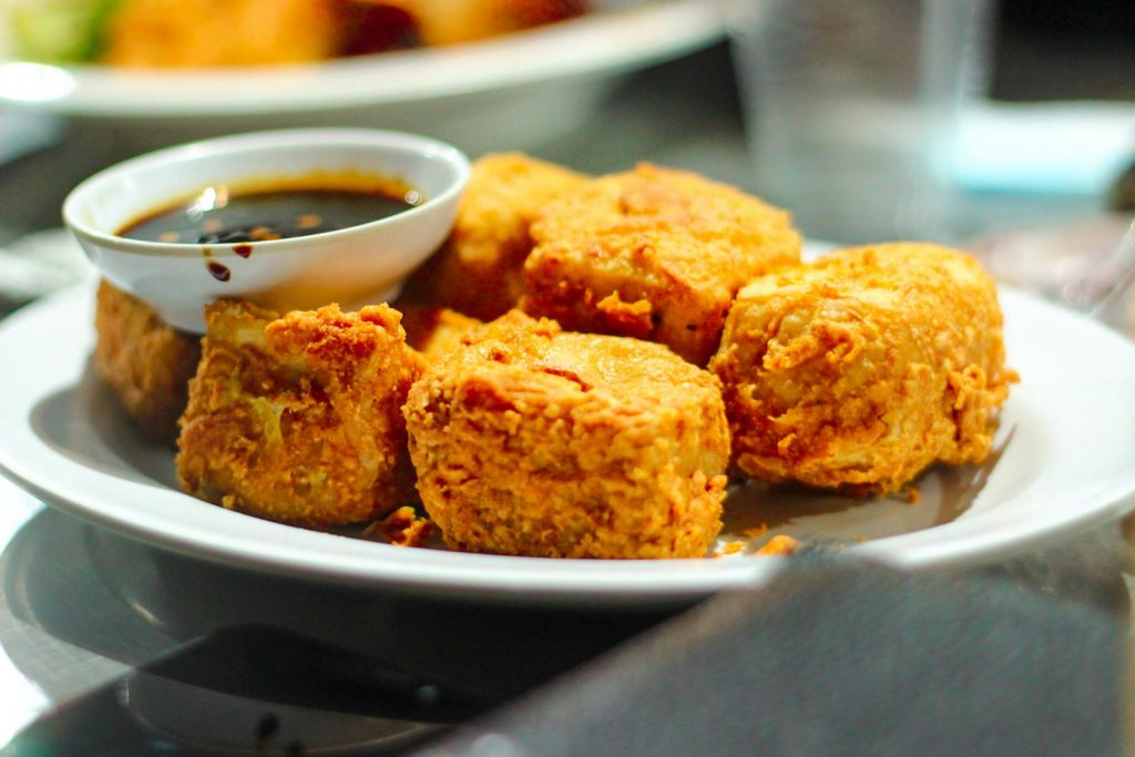 a white plate topped with fried food next to a bowl of dipping sauce