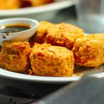 a white plate topped with fried food next to a bowl of dipping sauce